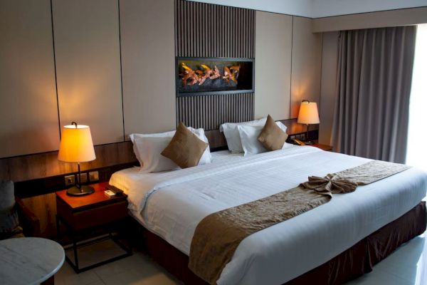 A cozy hotel room with a large bed, lamps on nightstands, a decorative piece on the wall, and curtains to the right.