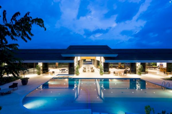 A luxurious building with open seating areas is illuminated at night, featuring a large, inviting pool in the foreground.