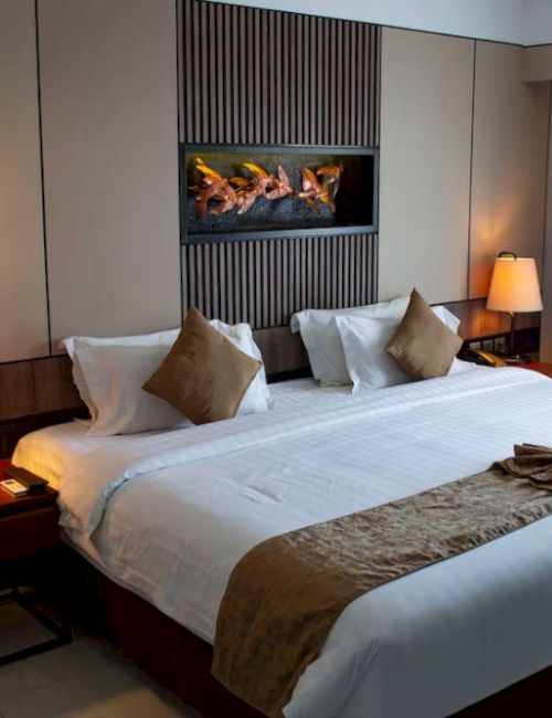 A modern hotel room with a large bed, decorative pillows, nightstands, lamps, and a wall-mounted art piece above the headboard.