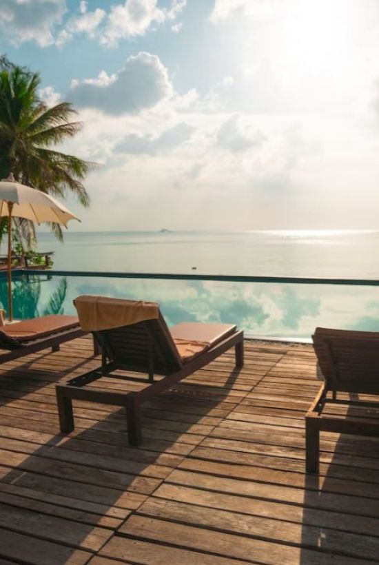 Beachside pool with lounge chairs, umbrellas, and palm trees under a bright sky. Serenity and relaxation by the water.
