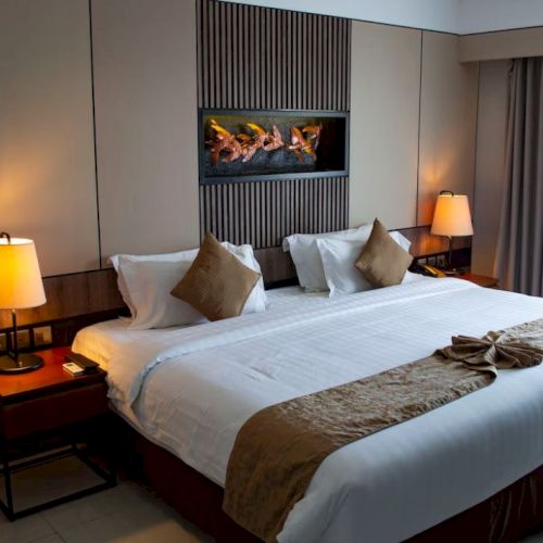 A hotel room with a large bed, decorative pillows, two bedside lamps, a wall art piece, and a window with curtains.