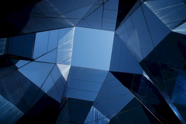 A view of the sky framed by reflective, modern glass architecture with angular designs and geometric patterns.