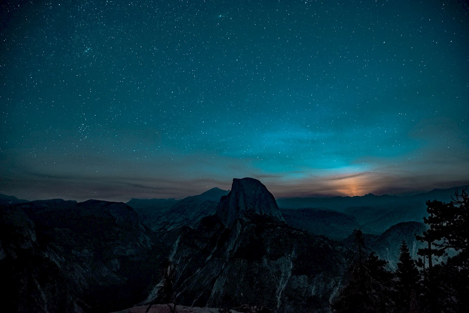 A mountainous landscape under a starry night sky, with a faint glow on the horizon, suggesting a moonrise or sunset.