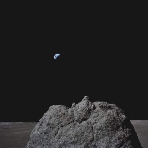 A rocky lunar surface with Earth visible in the distance against a dark sky.