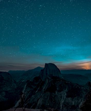 A starry night sky over mountains with a glowing horizon, creating a serene and mystical landscape scene.
