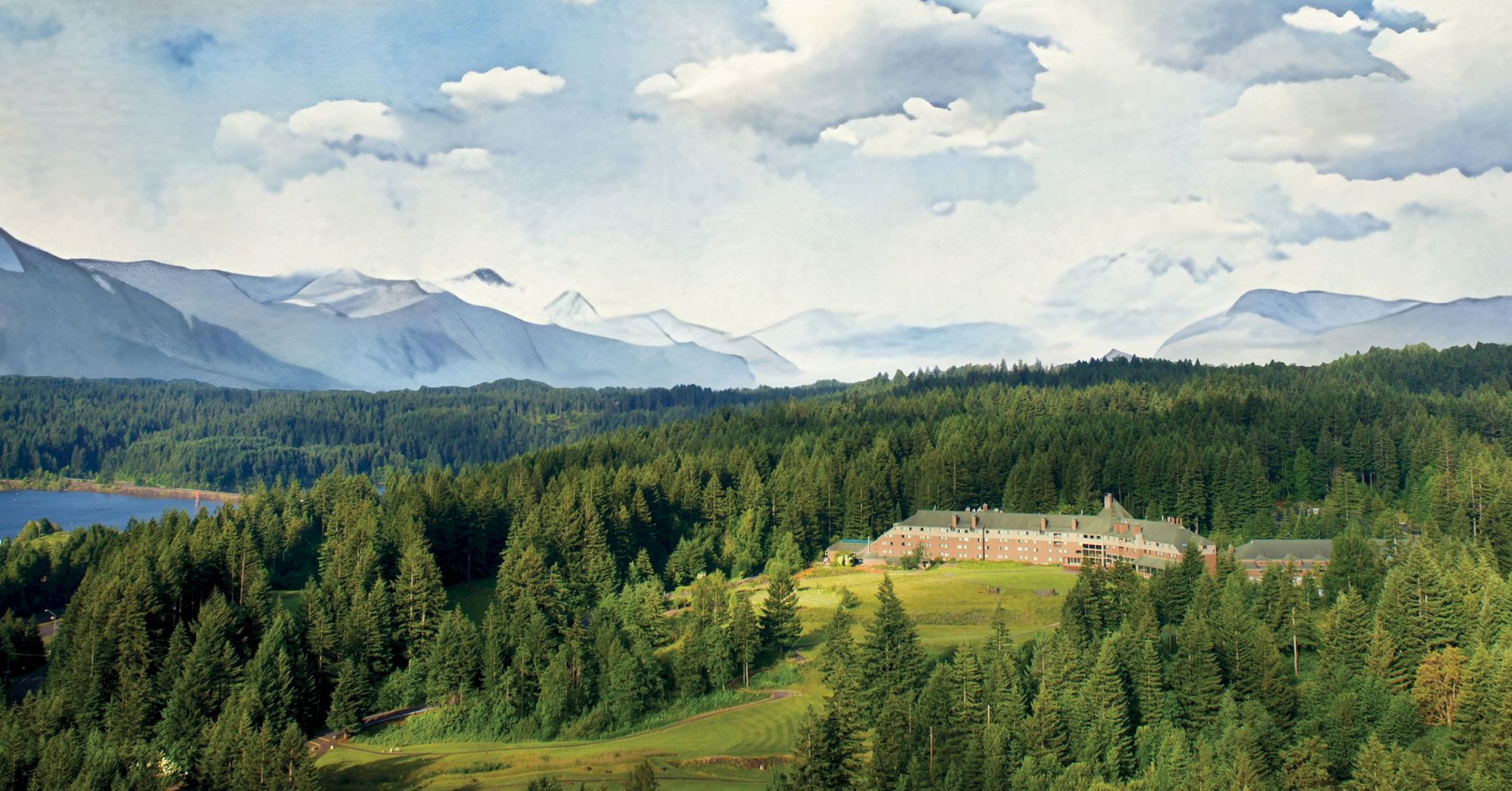 A large building surrounded by dense forest, with mountains and a lake in the background under a partly cloudy sky.