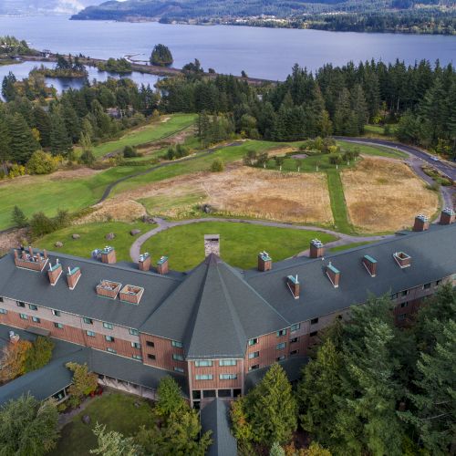 A large building surrounded by a forested area and a body of water in the distance.