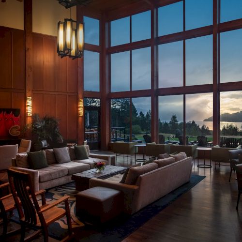 A cozy lounge with plush seating and large windows showcasing a scenic view of mountains and water during sunset.