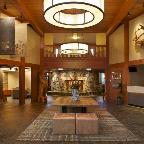 The image shows a hotel lobby with stone flooring, wooden accents, modern chandeliers, seating, and a stone fireplace in the background.