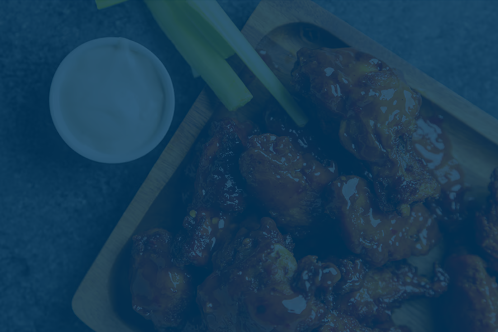 A plate of saucy chicken wings with celery sticks and a cup of dipping sauce on the side.