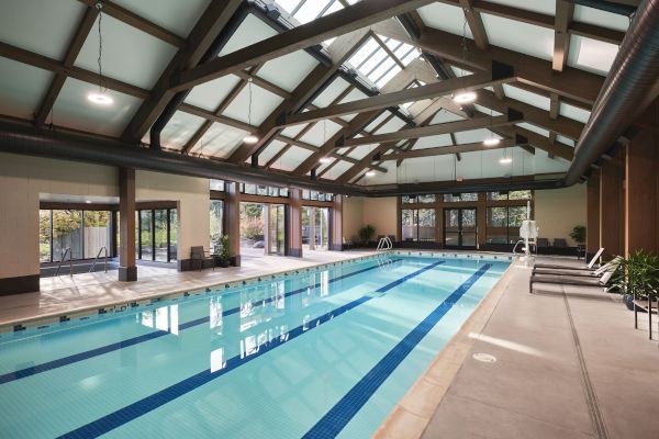 An indoor swimming pool with large windows, lounge chairs, and a high ceiling with exposed beams.
