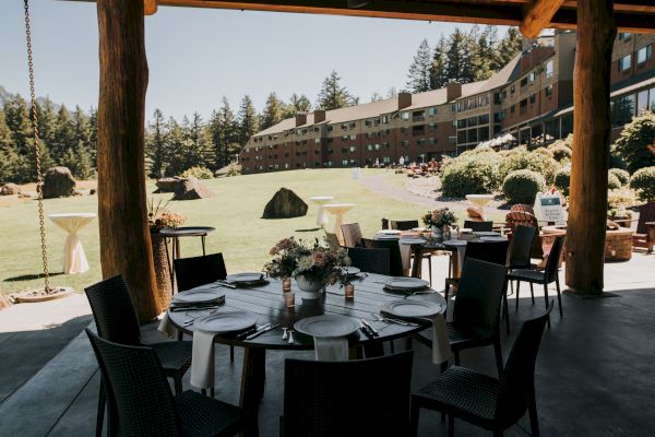 The image shows a decorated outdoor dining area with tables set, overlooking a grassy field and a large building in the background.