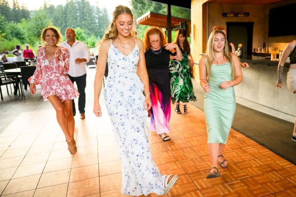 A group of people is dancing on a wooden floor, enjoying themselves in a lively setting with trees in the background.