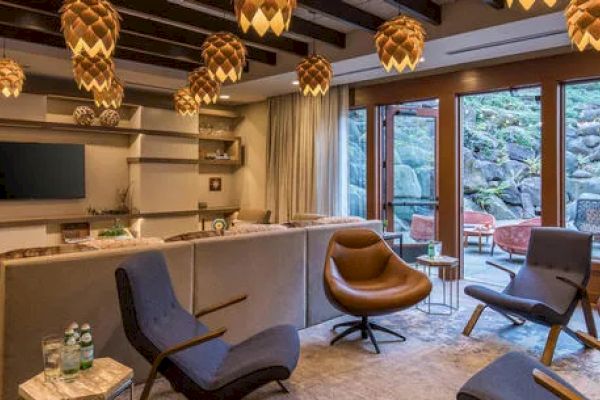 A cozy living room with modern furniture, pendant lights, a TV, and large windows overlooking a rocky outdoor area with seating.