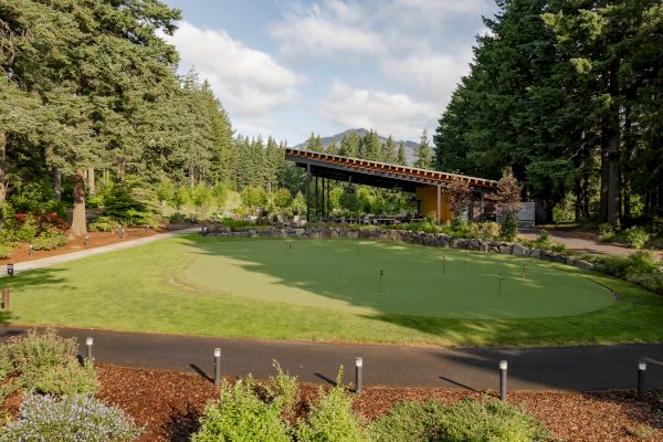 A landscaped area with a putting green, surrounded by trees and a modern canopy structure in the background.