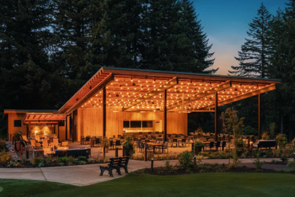 An outdoor pavilion with string lights, tables, and seating, surrounded by trees in a serene setting during twilight.