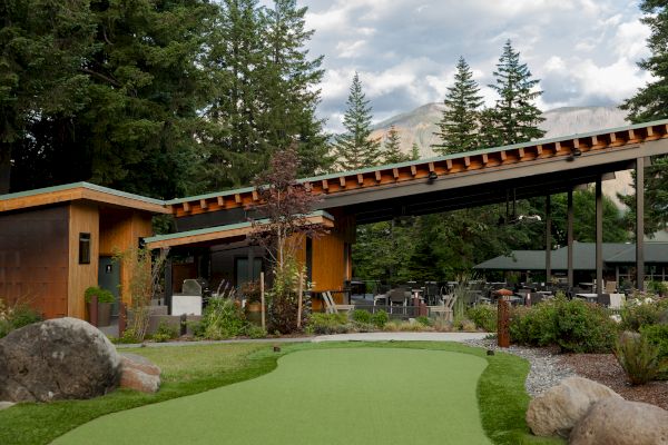 A modern building in a scenic setting with a green lawn and surrounding trees, under a cloudy sky, mountains in the background.
