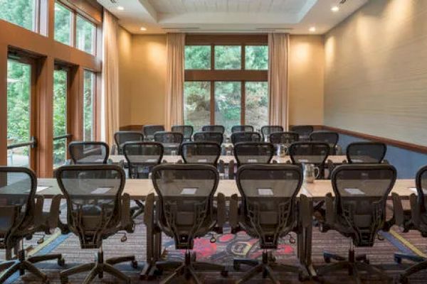 A conference room with tables, chairs, and natural light from large windows, set for a meeting with chairs facing the front.