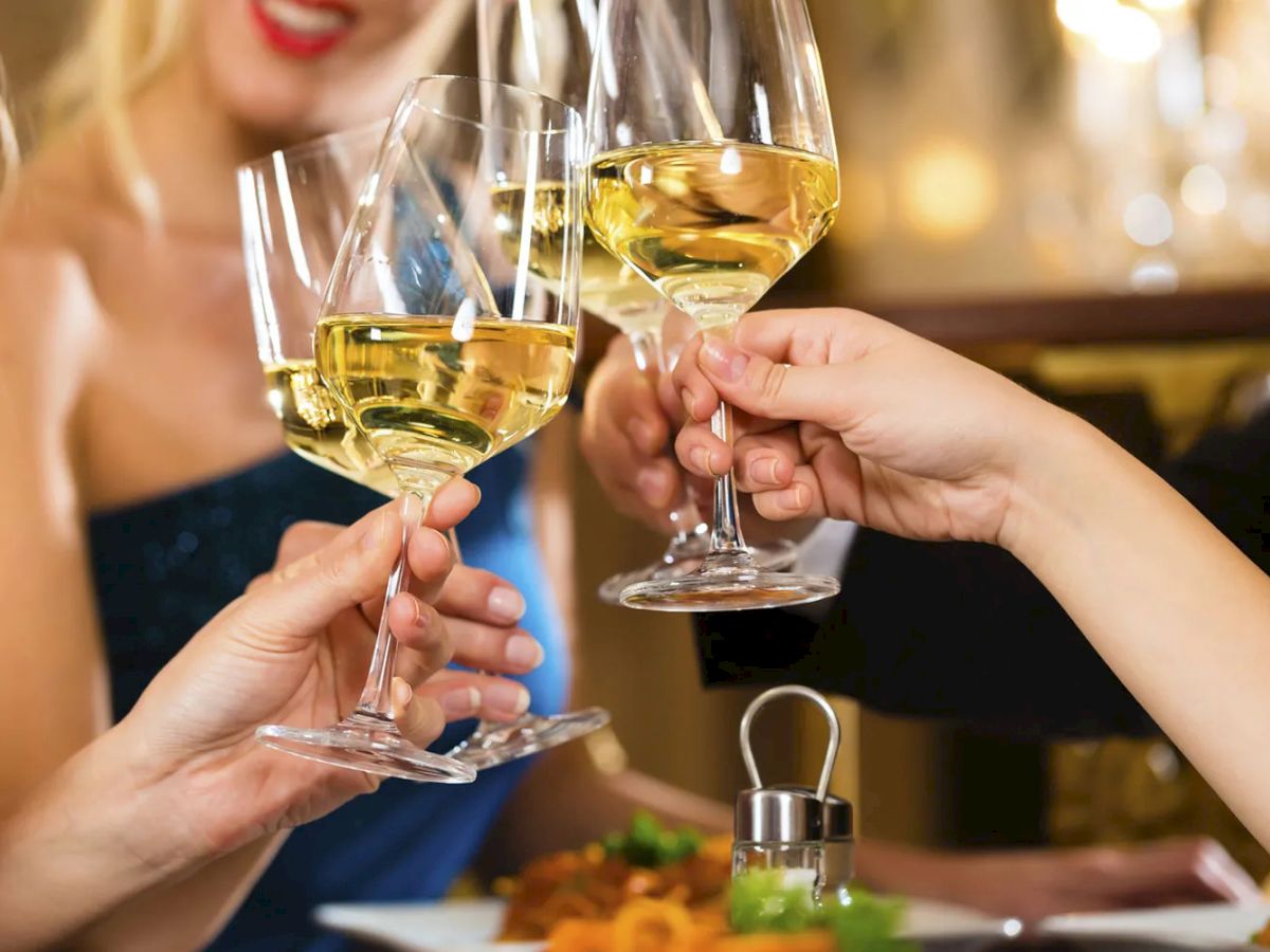 People clinking glasses of white wine in a celebratory setting, with a blurred background.