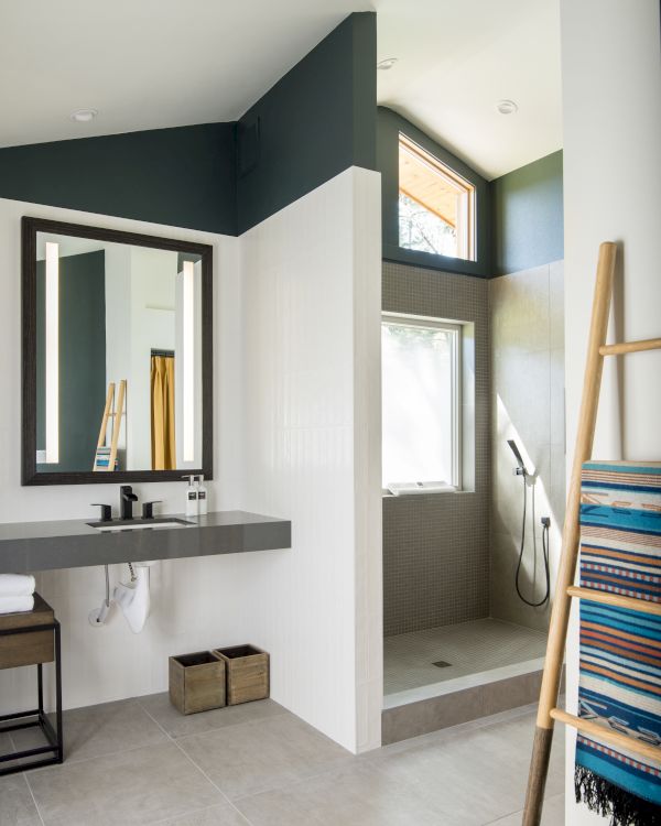 A modern bathroom with a shower, mirror, sink, ladder rack with towels, and natural light from a window.