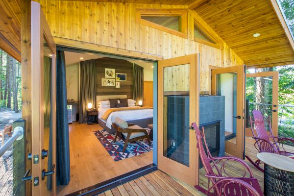 A serene cabin features an inviting bedroom with a large bed, a cozy porch with chairs, and lush greenery surrounding the space.