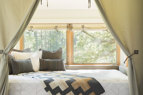 Cozy bed with geometric blanket and pillows, enclosed by drapes; large window offers a view of trees outside.