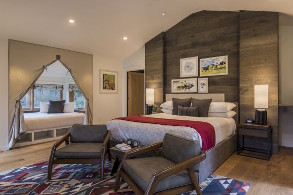 A cozy bedroom with a large bed, accent chairs, colorful rug, and alcove seating by the window, creating a warm and inviting atmosphere.