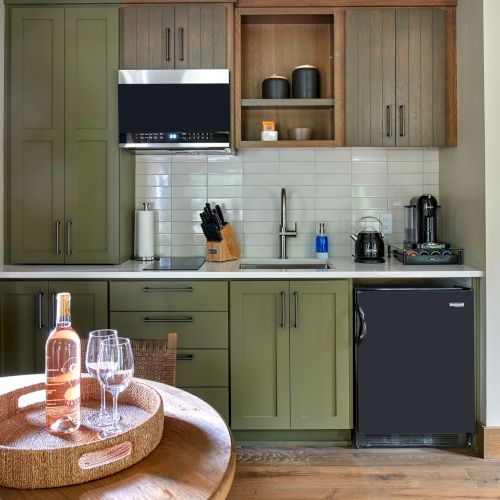 A modern kitchen with olive cabinets, a microwave, sink, espresso machine, and a table with wine and glasses on a tray.