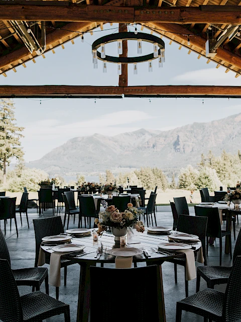 Outdoor dining area with round tables, set for an event. Features wooden beams and mountain views. Elegant and scenic setup for gatherings.