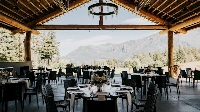 Outdoor dining area with round tables, set for an event. Features wooden beams and mountain views. Elegant and scenic setup for gatherings.