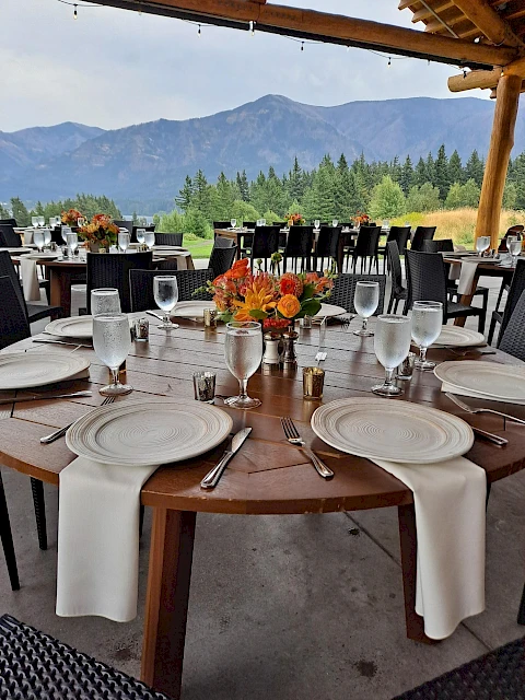 An outdoor dining setup with elegantly arranged tables, floral centerpieces, and mountain views in the background.