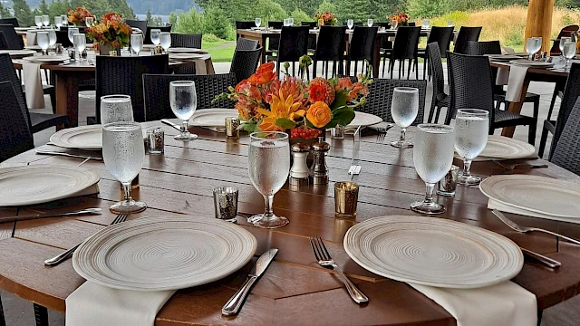 An outdoor dining setup with elegantly arranged tables, floral centerpieces, and mountain views in the background.
