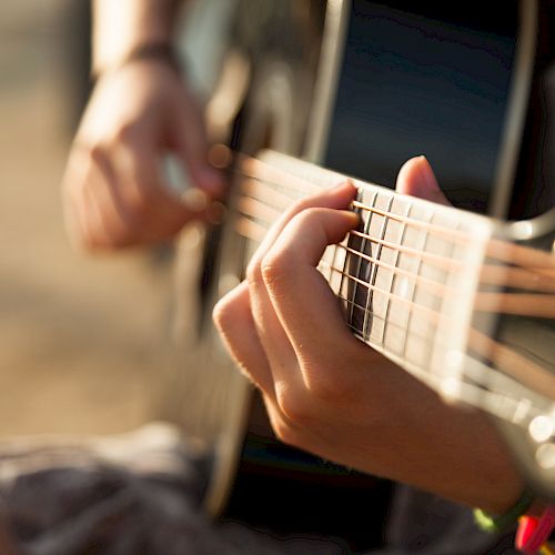 A person is playing an acoustic guitar, focusing on the strumming and fingering technique under natural lighting conditions.