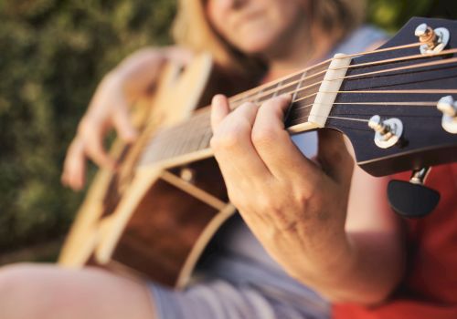 A person is playing an acoustic guitar outdoors, focusing on their hand on the strings.
