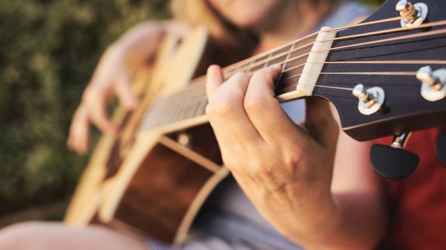 A person is playing an acoustic guitar outdoors, focusing on their hand on the strings.