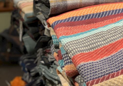 A stack of colorful, folded textiles or blankets with various patterns is displayed on a shelf.