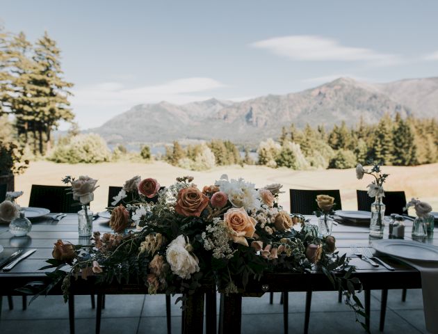 A beautifully set outdoor table with floral centerpiece, backed by a scenic view of mountains and trees on a clear day.