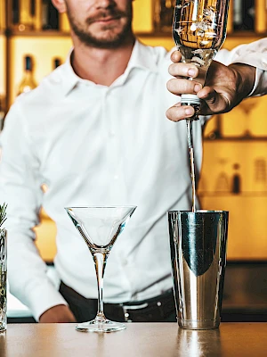 A bartender is making a cocktail with various ingredients and tools on the counter.