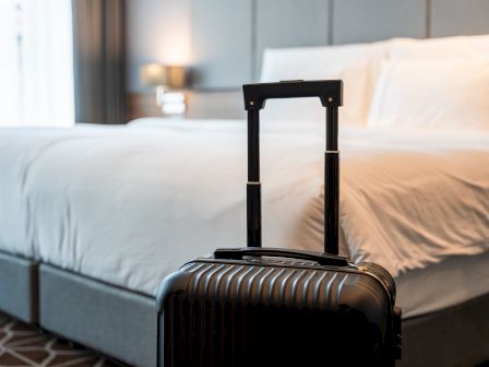 A suitcase stands in front of a neatly made bed in a hotel room, creating a tidy and inviting atmosphere.