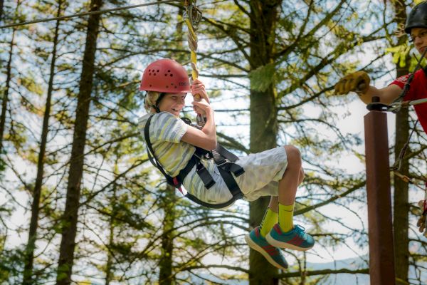 A person in a helmet and harness is enjoying a zip line ride amidst a forest, assisted by an instructor.