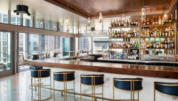 A chic bar with stylish stools, a well-stocked liquor shelf, and large windows offering a city view.