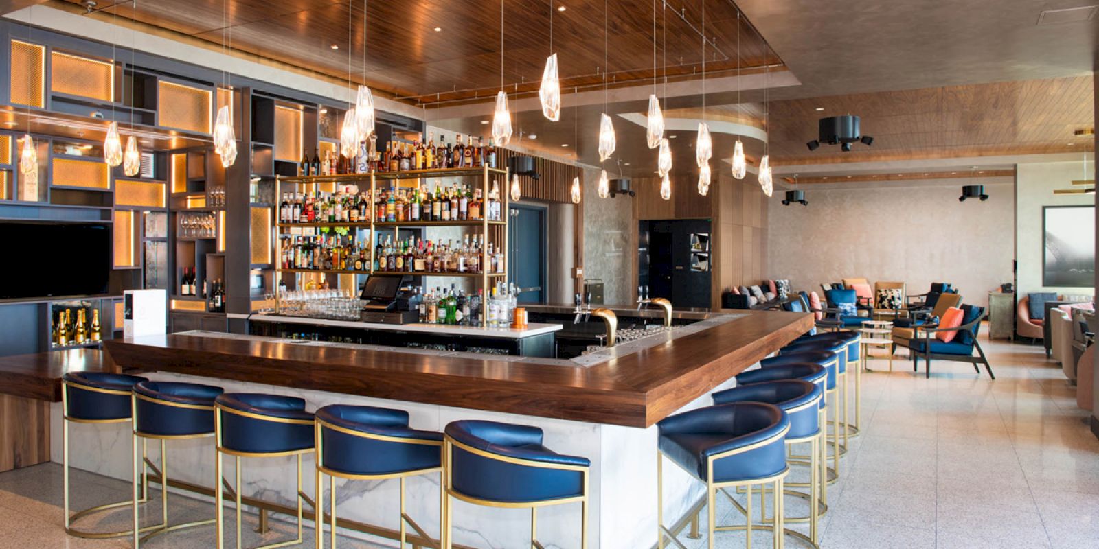 A modern bar with hanging lights, a well-stocked back shelf, and blue high chairs. The setting is stylish and inviting.