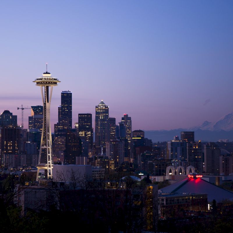 Seattle skyline at dusk, featuring the Space Needle, city buildings, and Mount Rainier in the background, under a clear sky.
