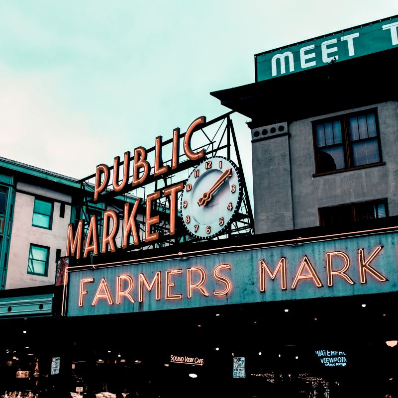 The image shows a neon sign for a "Public Market" and "Farmers Market" with a clock on a building, likely indicating a well-known market area.