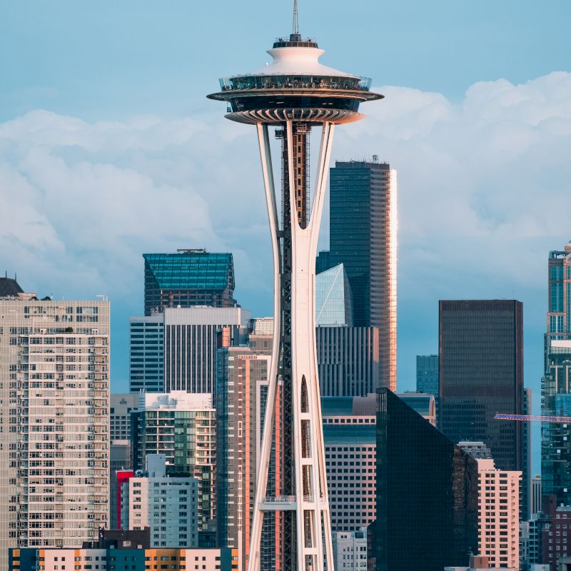 The image shows the Space Needle with a backdrop of skyscrapers, set against a partly cloudy sky in a cityscape scene.