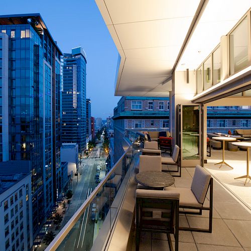A modern rooftop terrace at dusk, with outdoor seating and city buildings in view, creating a serene urban setting.
