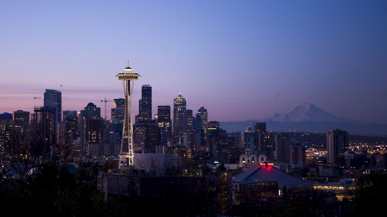 Seattle skyline at dusk, featuring the Space Needle with Mount Rainier visible in the background under a purple sky.